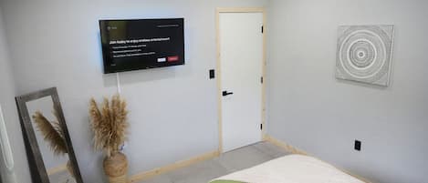 A bedroom with a bed, a television mounted on the wall, a door, and a decorative wall piece.