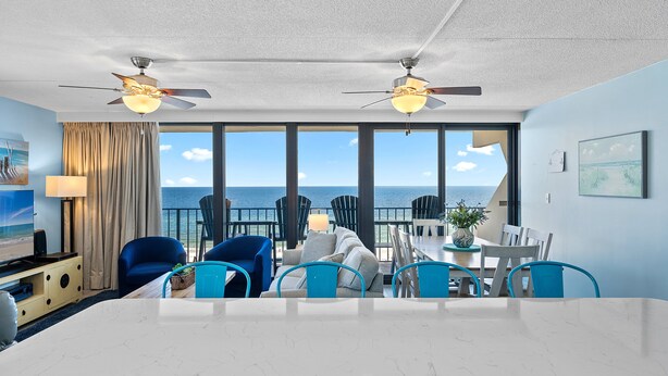 Ein modernes Hotelzimmer mit großem Esstisch, blauen Stühlen, einer Couch und einem Balkon mit Meerblick.