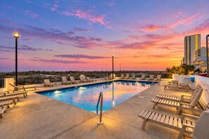 A rooftop pool with lounge chairs and a sunset view.