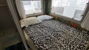 Una cama pequeña y acogedora con colcha de estampado de leopardo en una habitación compacta con ventanas.
