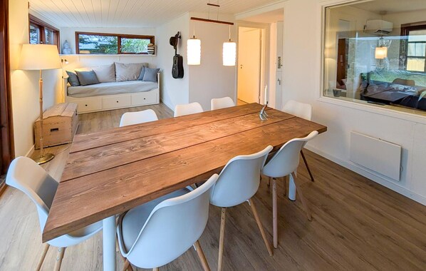 Een zithoek met een houten tafel en witte stoelen, een bank met kussens en een raam met uitzicht.