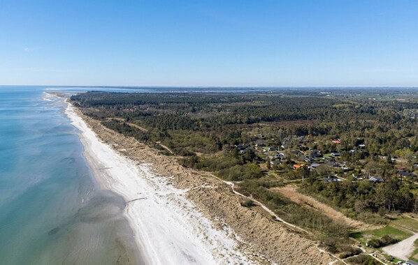 Vue aérienne d’une zone côtière comprenant une plage, une zone boisée et quelques bâtiments résidentiels dispersés.