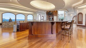 A spacious kitchen with a central island, wooden bar stools, and large windows offering ocean views. - Bay House by Avantstay Waterfront, Pier, Pond (Dameron)
