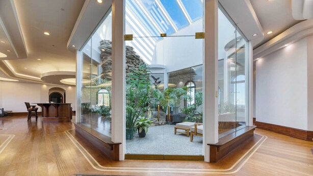 A spacious lobby with a glass wall leading to a lush indoor garden, wooden flooring, and a reception desk. - Bay House by Avantstay Waterfront, Pier, Pond (Dameron)