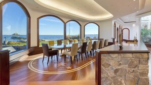 A spacious dining area with a long table and chairs, large windows offering a view of the sea, and a stone accent wall. - Bay House by Avantstay Waterfront, Pier, Pond (Dameron)