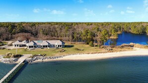 A large house with a dock extending into a lake, surrounded by trees and a clear sky. - Bay House by Avantstay Waterfront, Pier, Pond (Dameron)