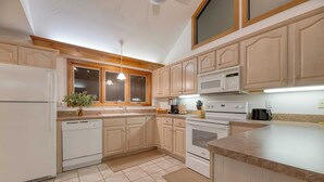 A kitchen with wooden cabinets, a white refrigerator, a microwave, an oven, and a sink. - Bay Cottage by Avantstay Waterfront, Pier, Pond (Dameron)