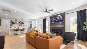 A modern living room with a brown sofa, a TV mounted on the wall, and a ceiling fan.
