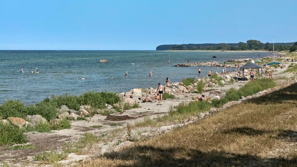 Una playa con costa rocosa, gente nadando y un barco en el agua.