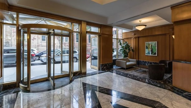 A lobby with a revolving door, marble flooring, a seating area, and a large window overlooking the street. - Walk to Central Park! Cozy 1BR w. AC, Wifi & Heating (New York)