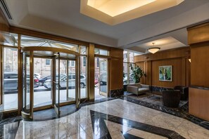 Um hall de entrada com porta giratória, piso de mármore, área de estar e uma grande janela com vista para a rua.