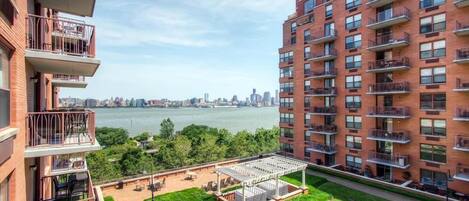 A high-rise apartment with multiple balconies, a rooftop garden, and a view of a river and city skyline.