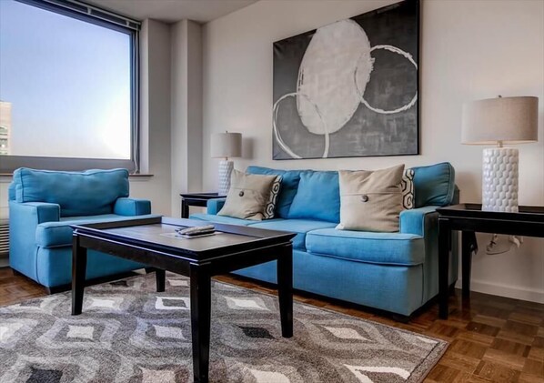 Una sala de estar moderna con un sofá azul, una mesa de centro y un cuadro abstracto grande en la pared.