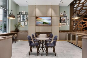 Un moderno comedor con una mesa redonda central rodeada de sillas, un televisor de pantalla plana montado en la pared y cuadros enmarcados en las paredes.