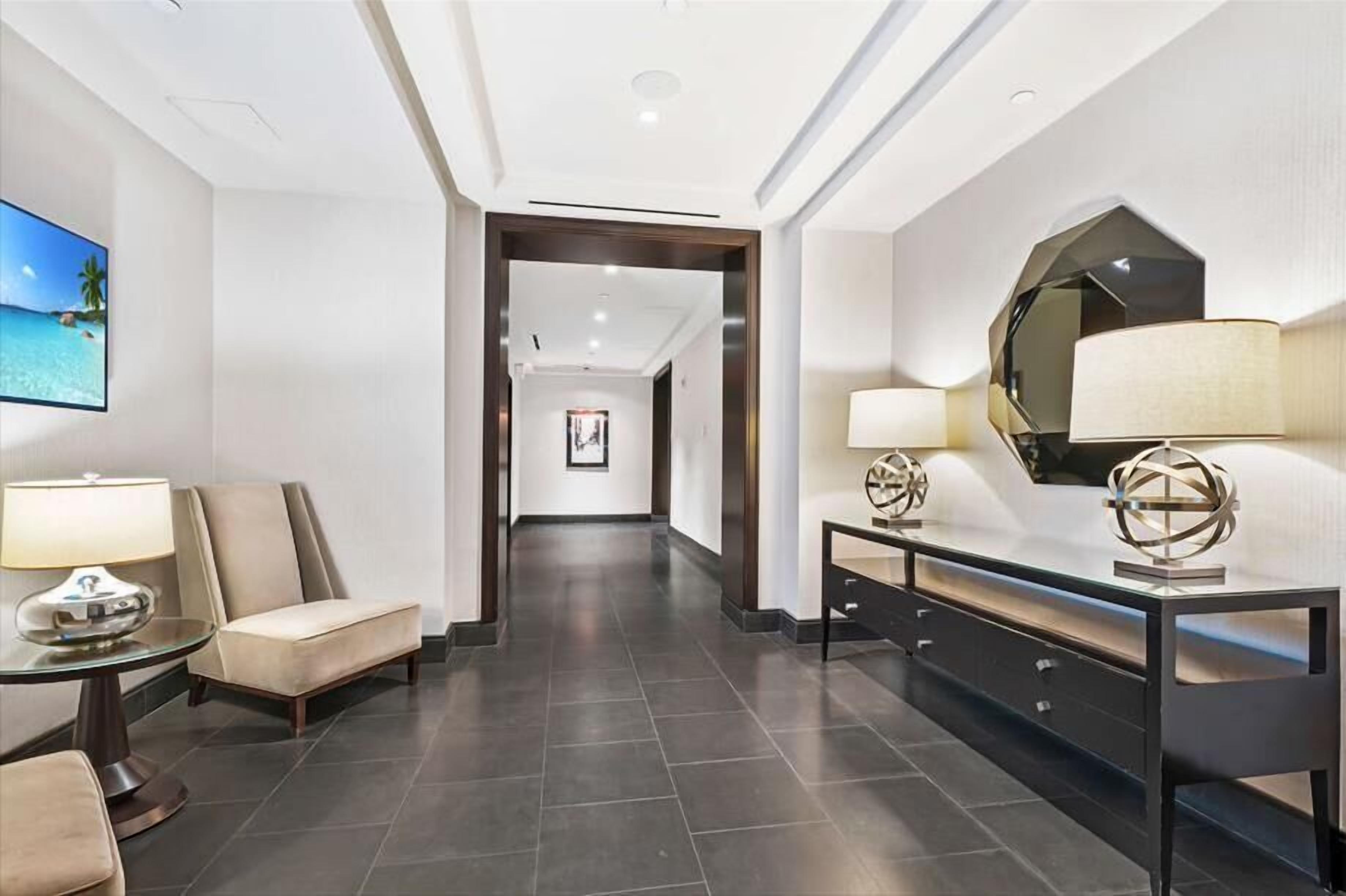 Eine Hotellobby mit modernem Design, die einen langen Gang, eine Sitzecke mit einer Couch und einem Tisch sowie einen Konsolentisch mit Dekorationen zeigt.
