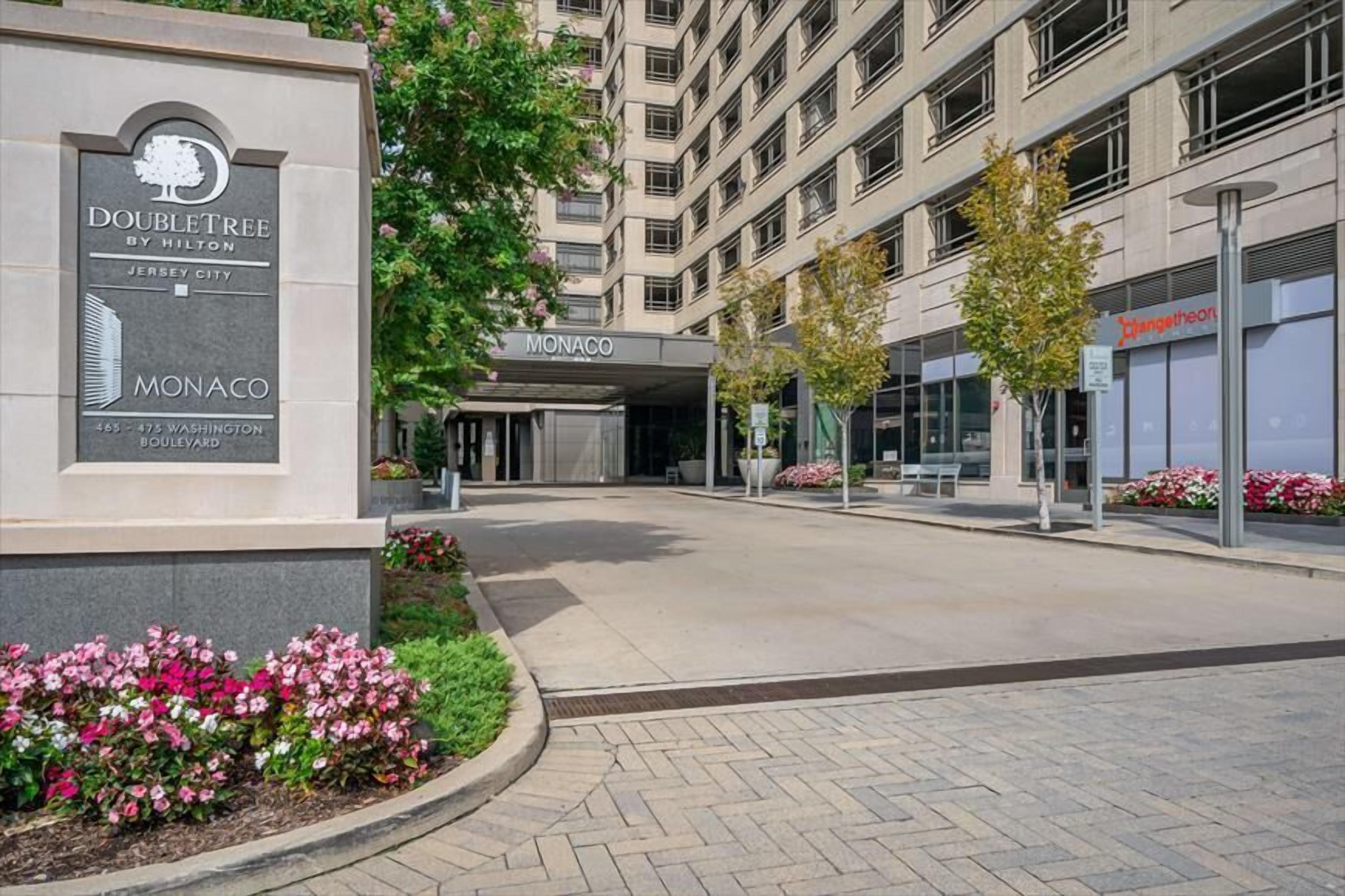 A DoubleTree by Hilton hotel entrance with a sign for Monaco, a paved walkway, and surrounding greenery.