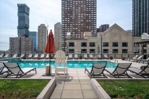 A rooftop pool with lounge chairs and a view of city buildings.