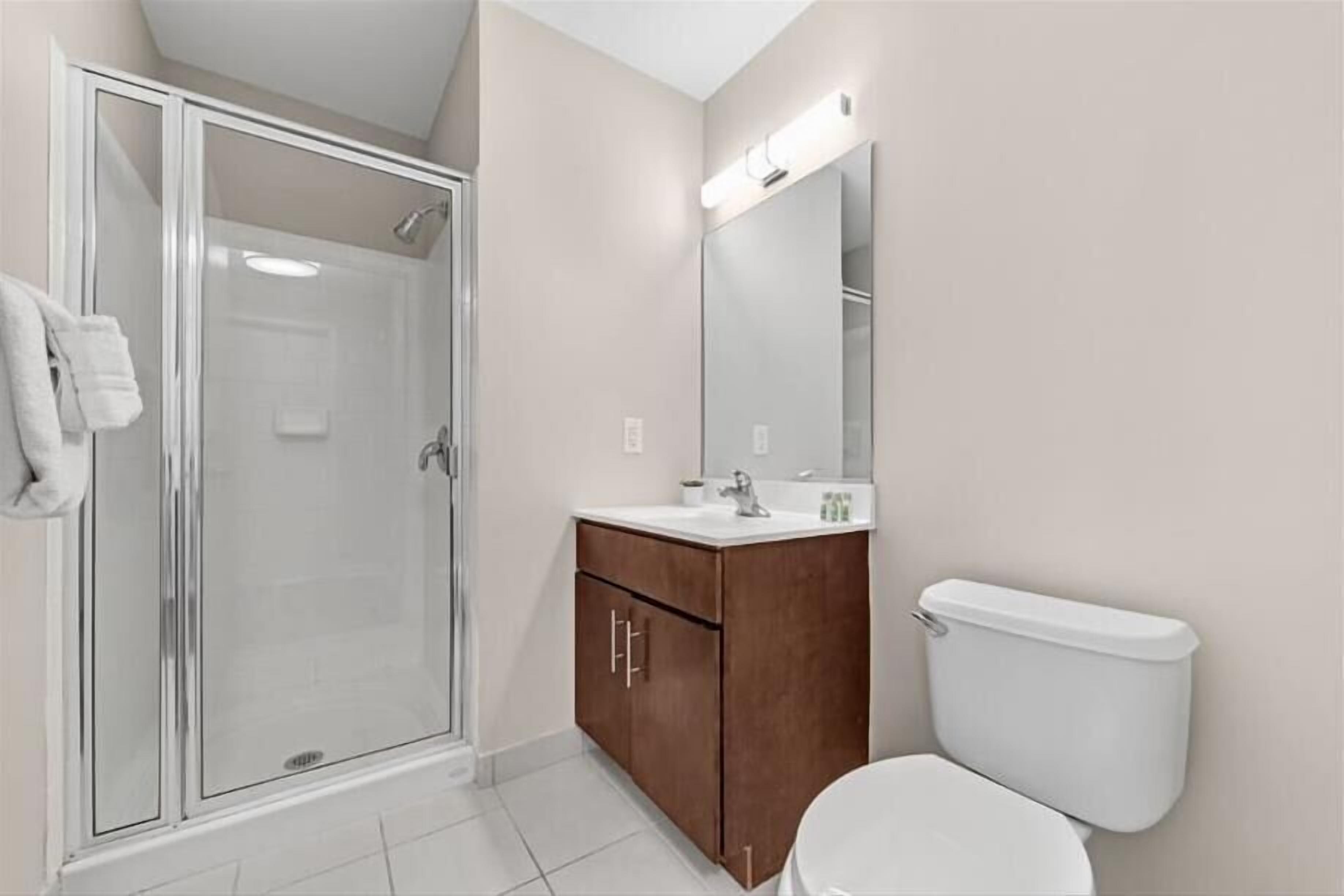 Un baño con cabina de ducha de vidrio, tocador de madera, inodoro blanco y un espejo grande.