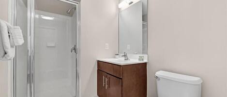 Un baño con cabina de ducha de vidrio, tocador de madera, inodoro blanco y un espejo grande.