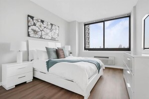 A modern bedroom with a large bed, white nightstands, a large window with a city view, and a decorative wall piece.