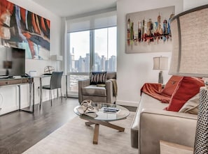 Una sala moderna con una mesa de centro de vidrio, un sofá, un comedor con una silla y vistas a la ciudad a través de amplios ventanales.