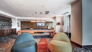 A modern hotel room with a pool table, two armchairs, a bar area, and a large window. - Modern Jersey City 1BR | Work Desk + Wi-Fi | by GLS (Jersey City)