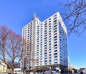 A multi-story building with a modern architectural design, featuring numerous windows and a prominent corner structure. - City View 2BR near Boston skyline (Cambridge)