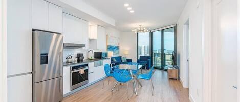 A modern kitchen with white cabinets, a stainless steel refrigerator, and a dining area with blue chairs.