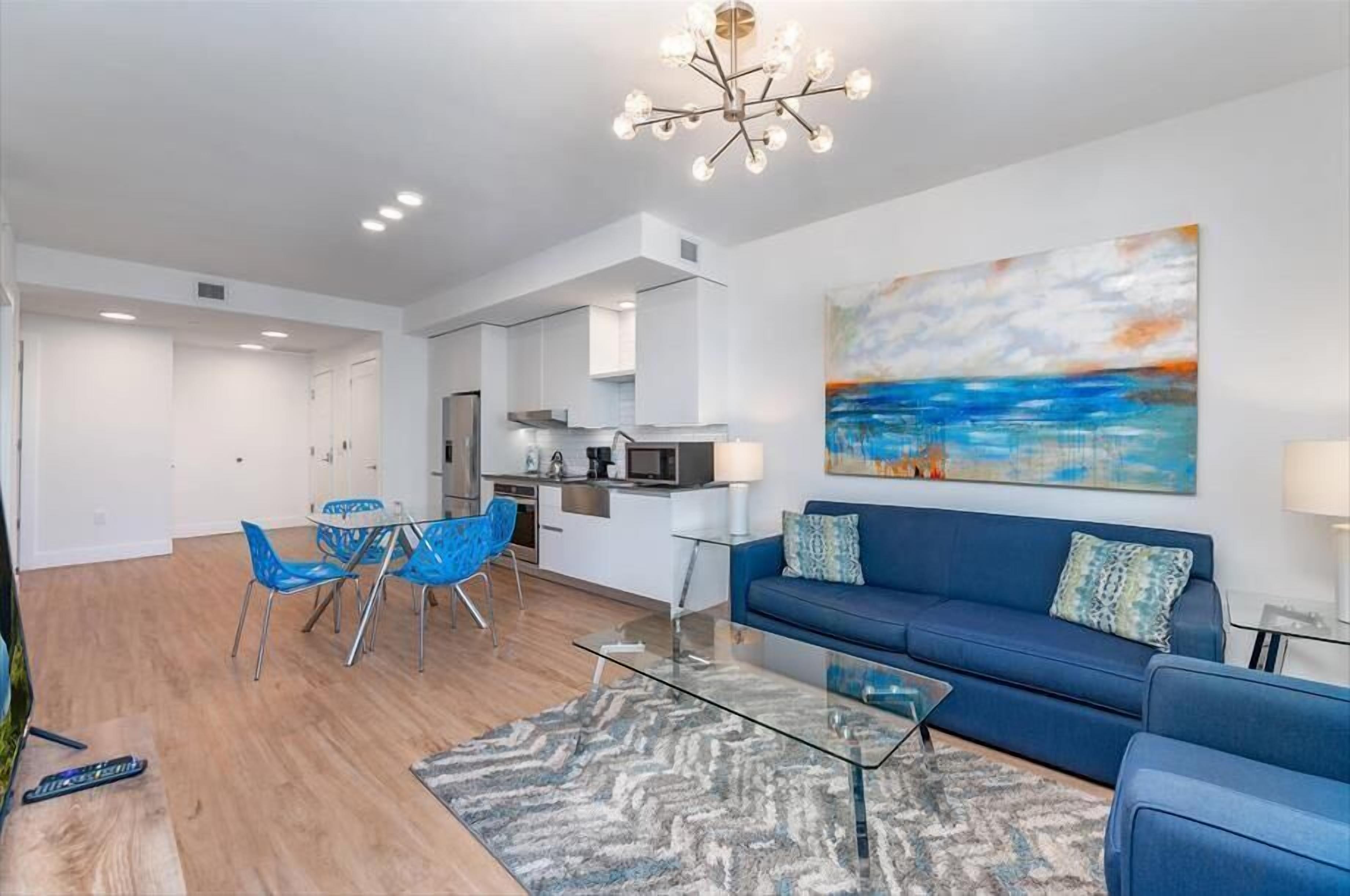 Un salon moderne avec un canapé bleu, une table basse en verre et un coin repas avec des chaises bleues.