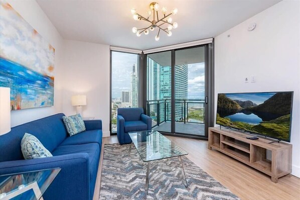 A modern living room with a blue sofa, a glass coffee table, and a television on a wooden stand.