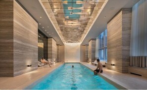 An indoor swimming pool with a modern design, featuring a wooden floor and walls, and a ceiling with a unique light fixture.