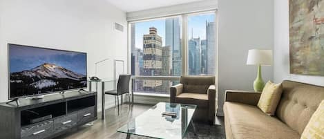 A modern living room with a large TV, a glass coffee table, a sofa, and a view of city buildings.