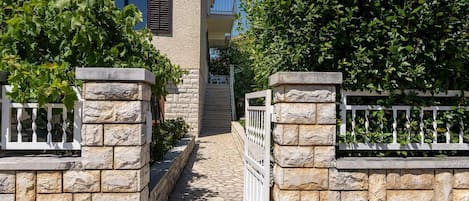 A stone-walled pathway leading to a building with a balcony.