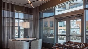 Una habitación moderna con una mesa de fútbol de mesa, una mesa redonda con sillas y ventanas amplias que ofrecen vistas de la ciudad.