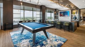 Una habitación moderna con mesa de billar, zona de bar y amplios ventanales con vistas a la ciudad.