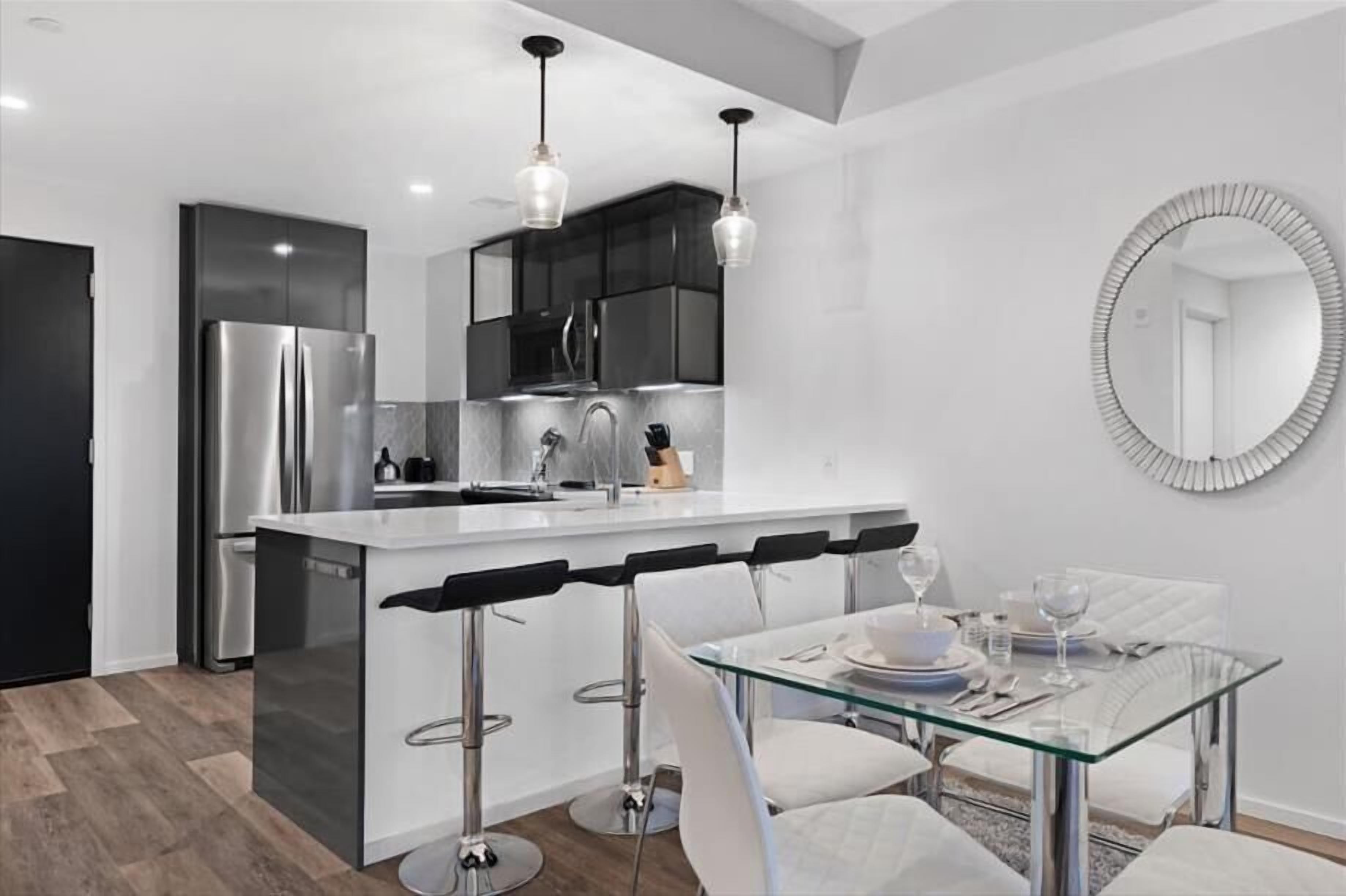 A modern kitchen with a central island, stainless steel appliances, and a glass dining table with bar stools.