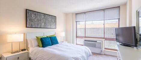 Habitación de hotel con cama, mesitas de noche, televisor y un ventanal con vista a un balcón.