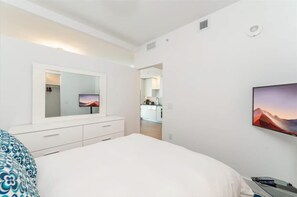 Une chambre à coucher moderne avec un grand lit, un téléviseur fixé au mur et un dressing.