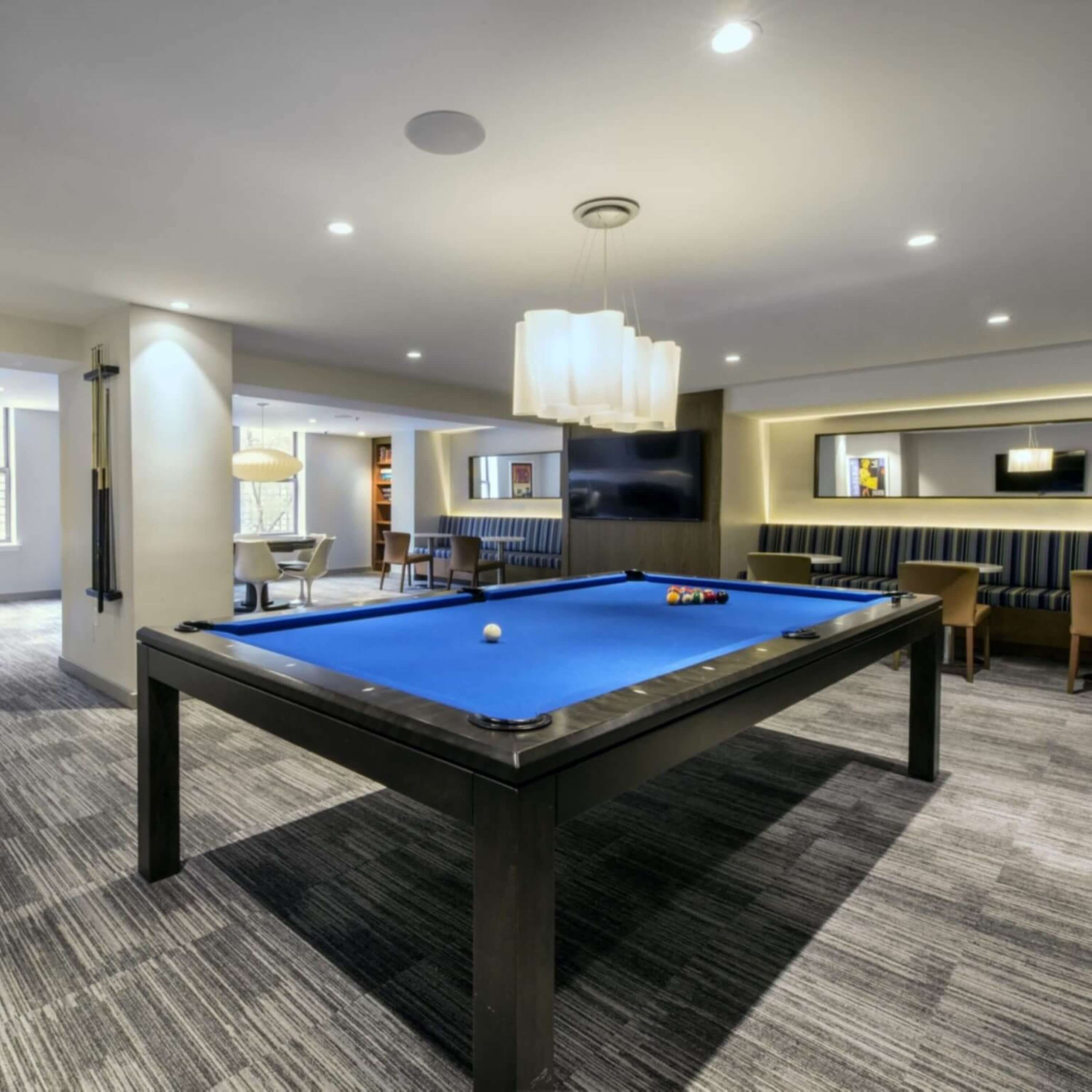 Mesa de bilhar num quarto moderno com televisão de tela plana, assentos confortáveis e espaço de bar.