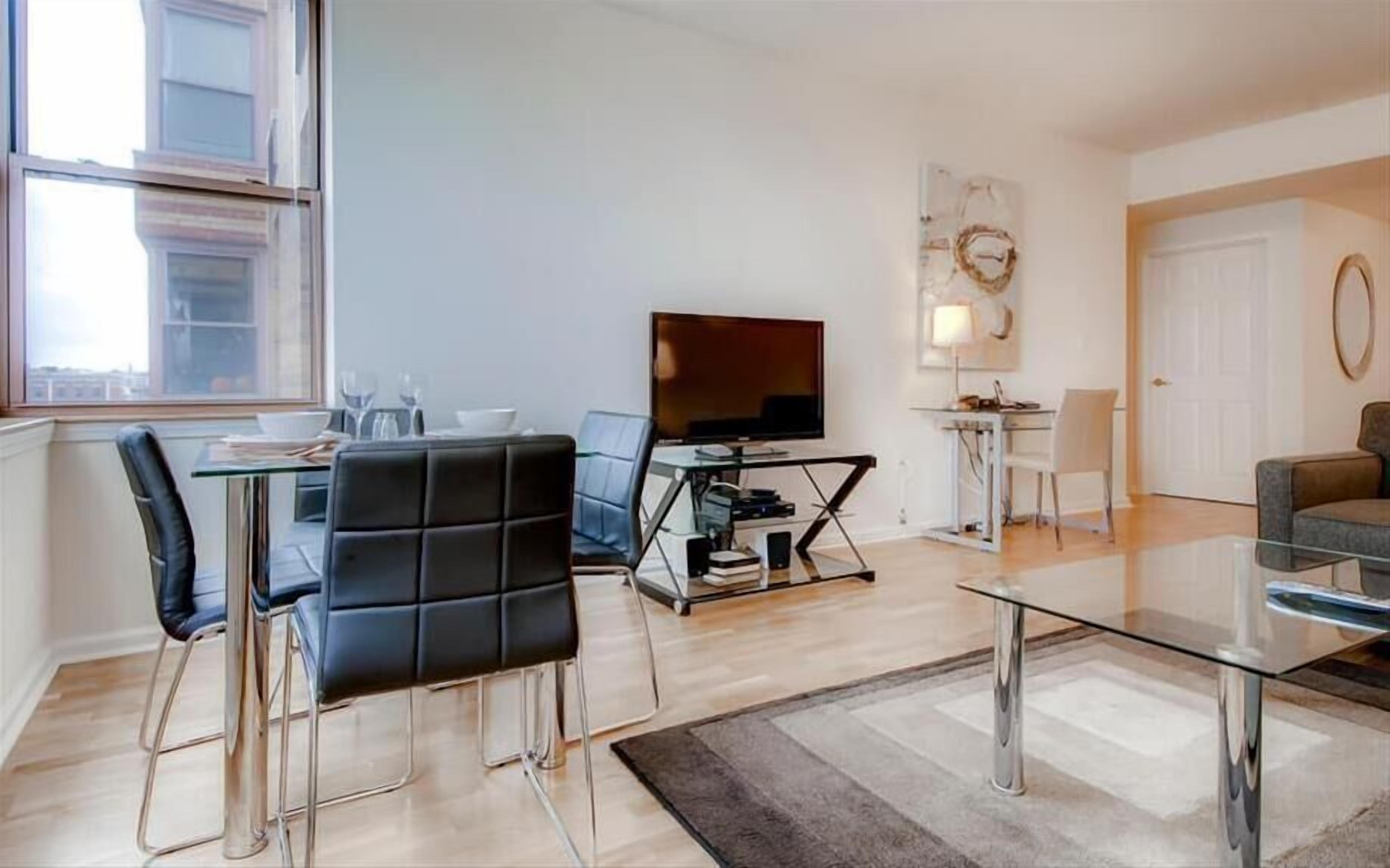 A modern living room with a glass coffee table, a flat-screen TV, and a dining area with a glass table and chairs.