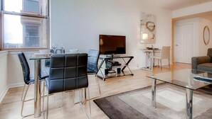 Un salon moderne avec une table basse en verre, un téléviseur à écran plat et un coin repas comprenant une table et des chaises en verre.