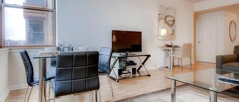 A modern living room with a glass coffee table, a flat-screen TV, and a dining area with a glass table and chairs.