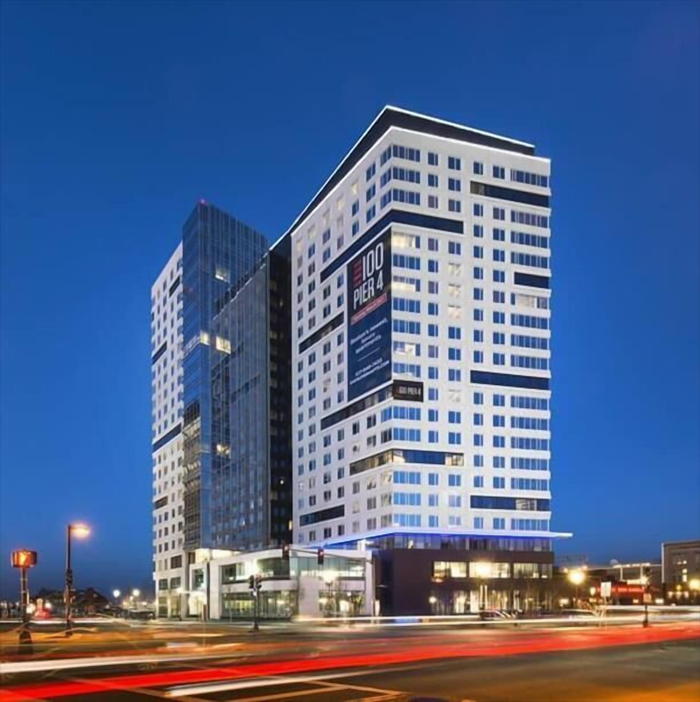 A modern hotel with a prominent '100 Pier 4' sign, featuring a mix of glass and white facade, and a corner location with a visible entrance.