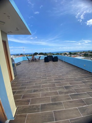 A rooftop terrace with a blue railing, a tiled floor, and outdoor furniture. - RESIDENCIAL DOÑA GLORIA III (Puerto Plata)