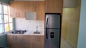 Une cuisine moderne avec des meubles en bois, un réfrigérateur en acier inoxydable, une cuisinière à gaz et une fenêtre qui laisse entrer la lumière naturelle.