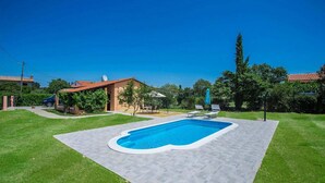 A residential backyard with a swimming pool, a patio area, and a small garden.