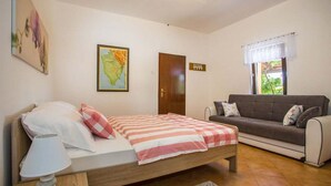 A bedroom with a bed, a wooden nightstand, a lamp, a map, a door, and a sofa.