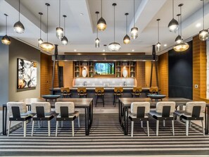 En modern hotellobby med en central bardisk, flera olika sittgrupper och hängande lampor.
