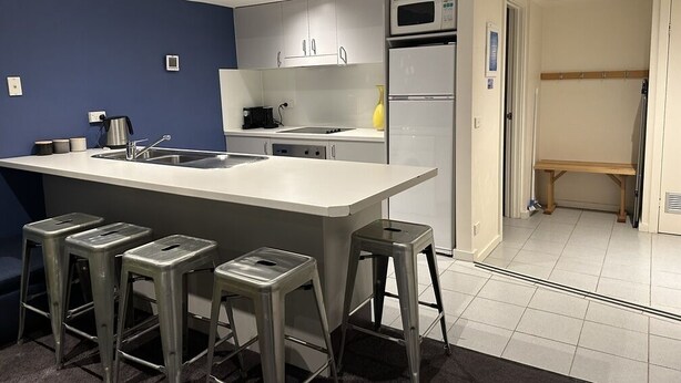 Moderni keittiö, jossa on keskeinen keittiösaareke, baarituolit, mikroaaltouuni ja jääkaappi.