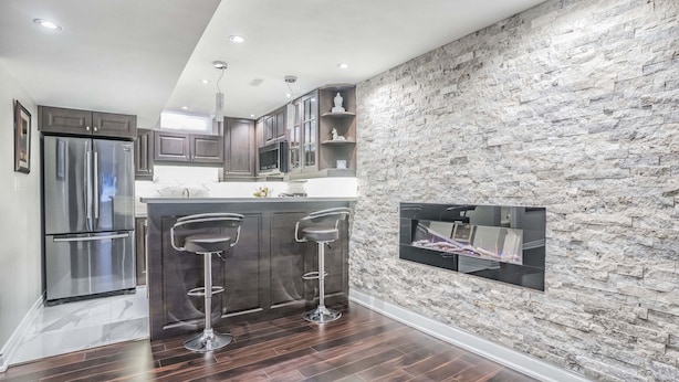 A modern kitchen with dark wood flooring, stainless steel appliances, and a stone accent wall. - Charming basement retreat awaits you! (Markham)